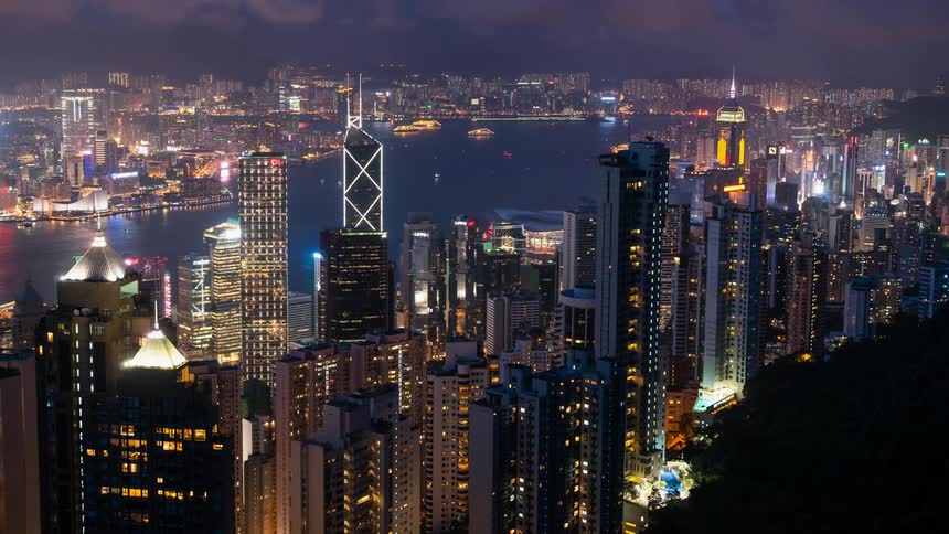 Boats floating down a river lined with skyscrapers in Hong Kong