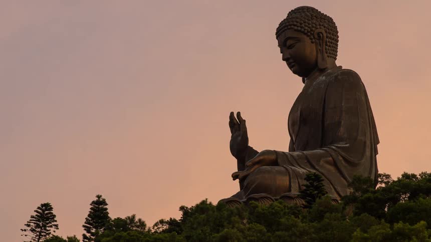 A large statue of buddha sits on top of a hill at sunset
