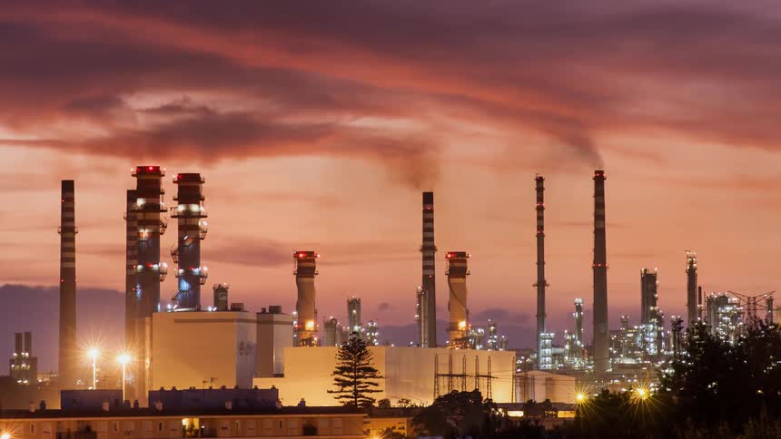 Smoke coming out of smokestacks near buildings at sunset
