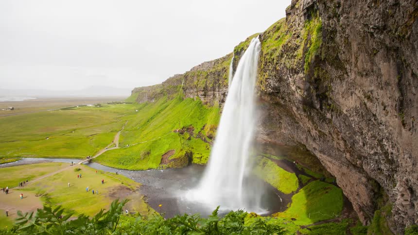 Time lapse of a huge waterfall and a lush green pasture beyond