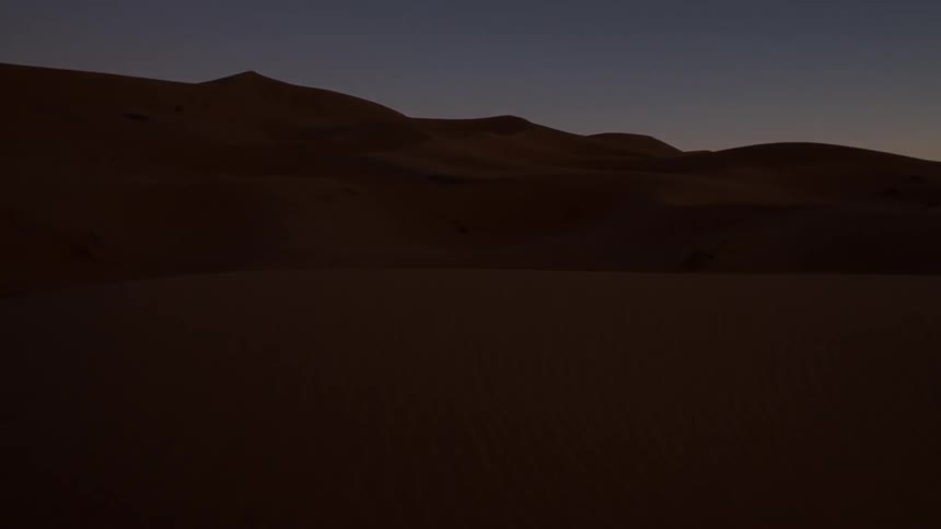 Wind blown sand dunes are covered in darkness as the sun sets