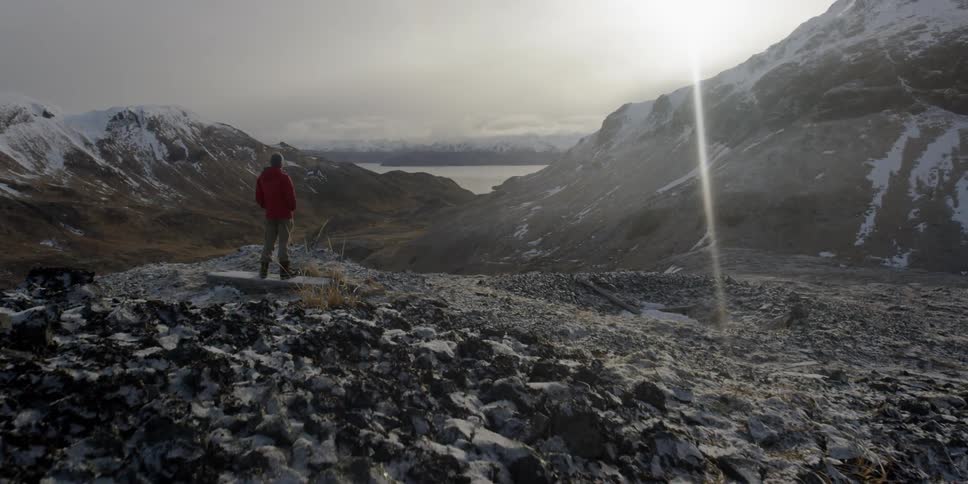 A man stands atop a mountain as the sun shines