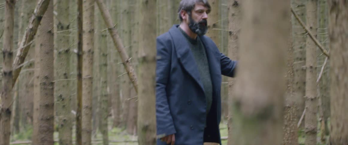 A man walks with his head down through the woods
