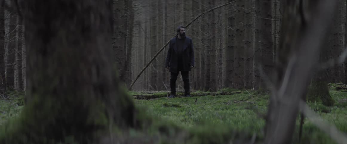A man steps over a fallen log and changes direction in a forest