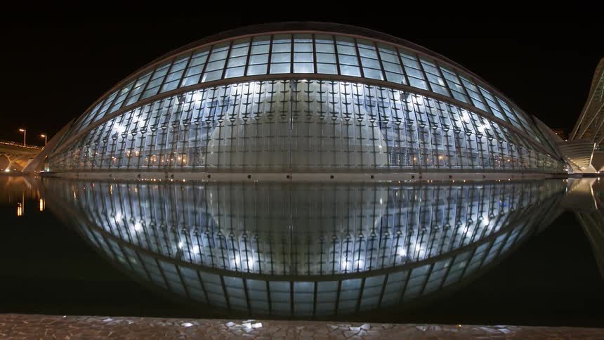 The shape of a building is reflected in a body of water at night