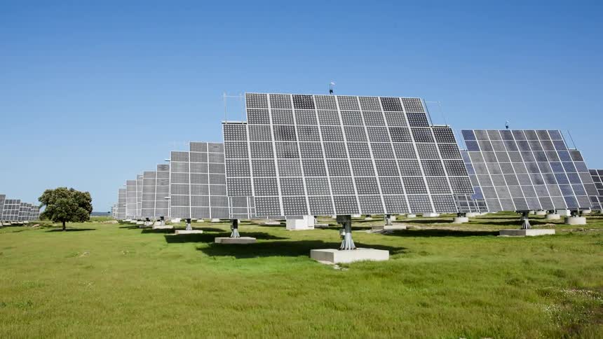 Wind blows through grass in a field with solar panels