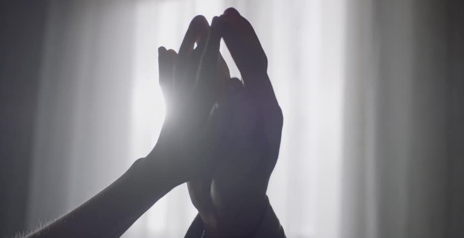 Two people touch hands together as the sun filters through curtains