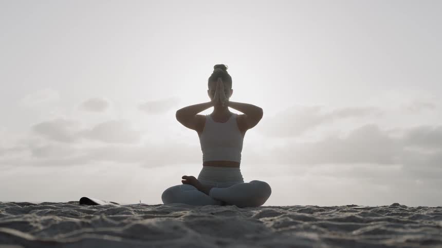 A woman does yoga on a beach at sunset
