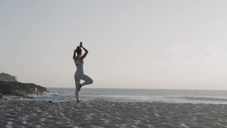 A woman is doing yoga on the beach