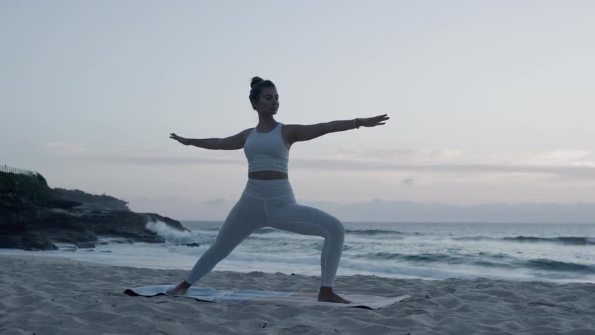 A woman stretches on a mat on the beach