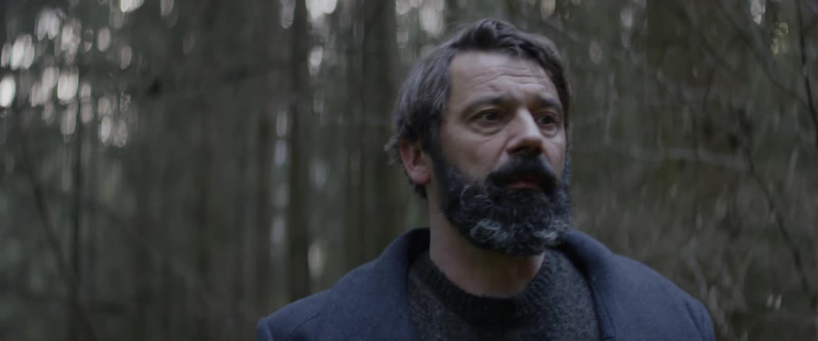 A man ducks his head under branches in the woods