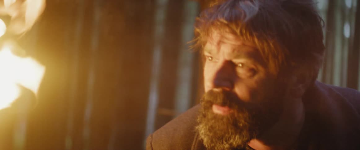 A man is holding a torch and looks lost and scared in the woods