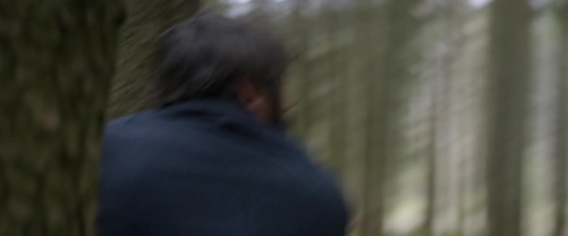 A man in the woods with a beard appears to be lost and scared