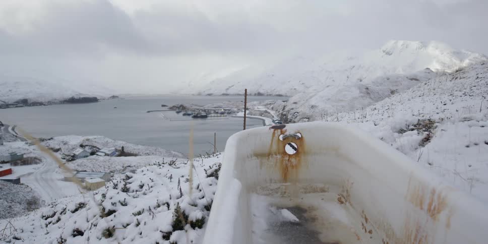 A bath tub sits on top of a snow covered hill overlooking a body of water