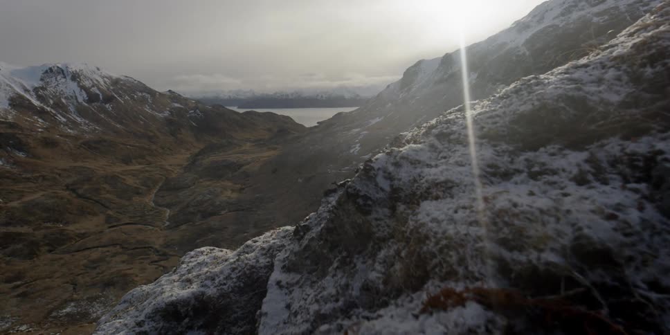 Sun shines over snowy mountains and a body of water