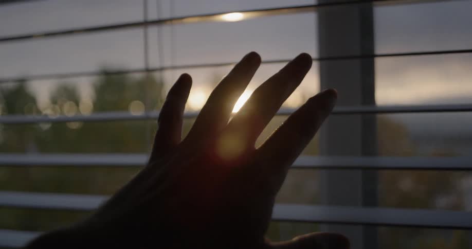 A person reaches their hand on blinds on a window