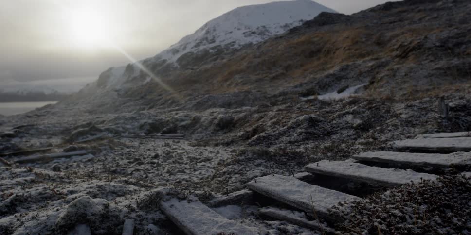 Sun rises over snowy mountains and decaying wood structure