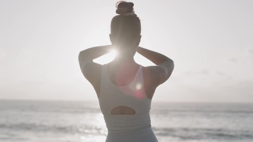 A woman in white clothing is doing yoga on the beach