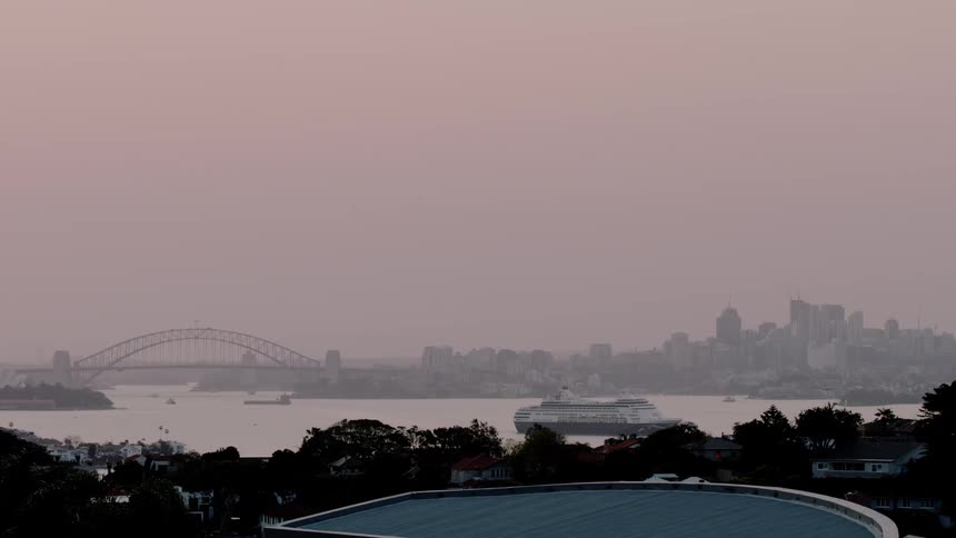 A ship moves out of a city harbor at sunset