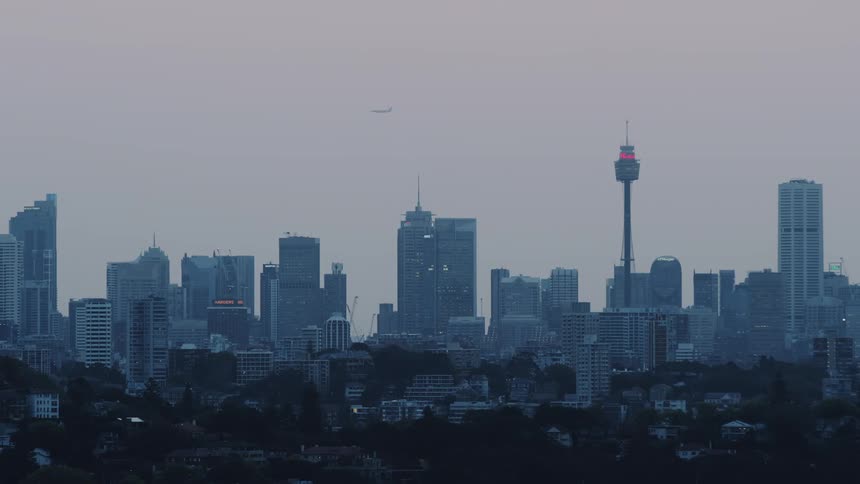 A plane flies high over the city buildings