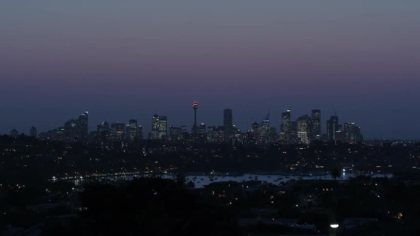 Lights from moving traffic and windows glow in a city skyline