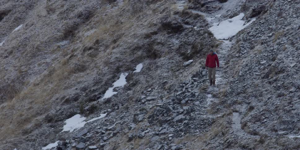 A man in a red jacket is hiking along a rocky cliff side