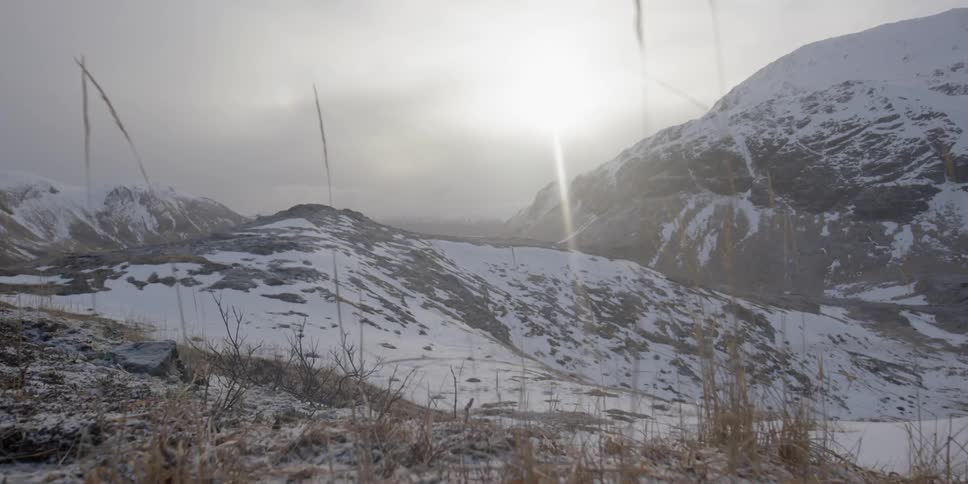 The sun shines through the clouds onto snow covered peaks