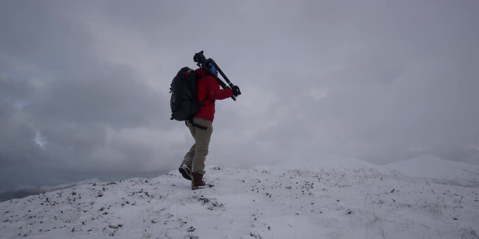 A man is hiking up the snow covered hill with a tripod