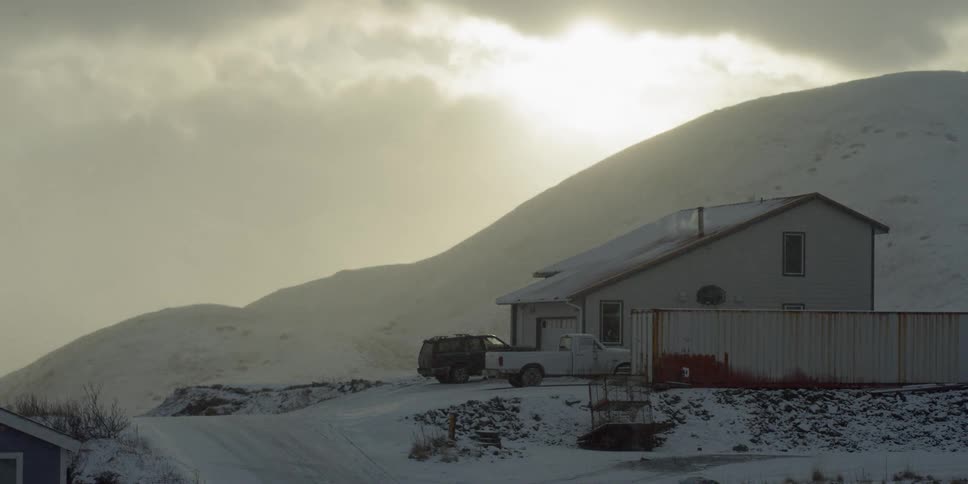 Trucks are parked in the driveway of a house on a snowy ridge