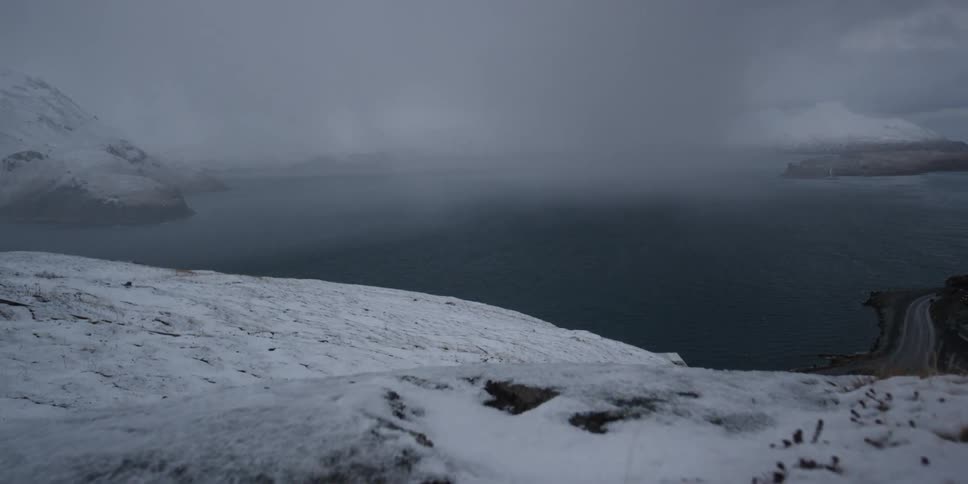 The wind blows the grass sticking out of the snow on the hill