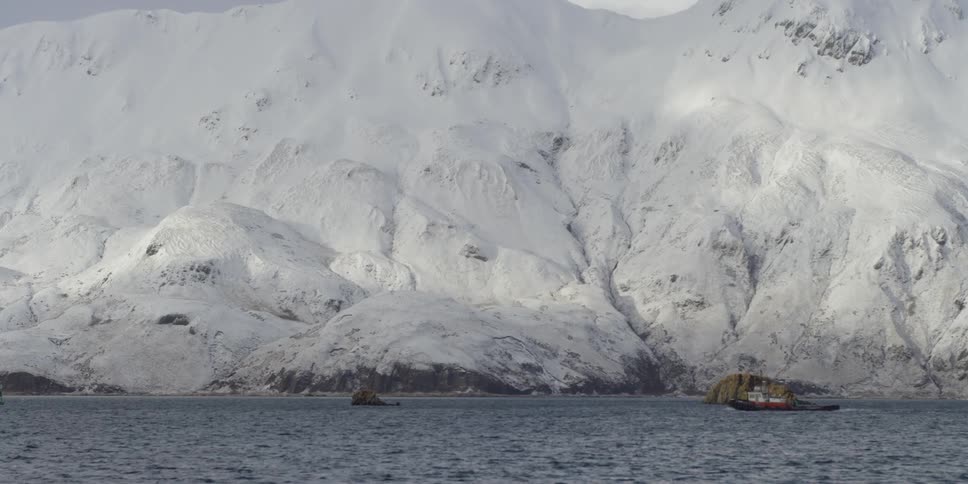 A tugboat sails past the large snow covered mountain