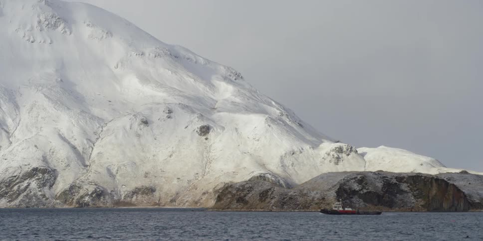 Boat floats in a large body of water in front of large snowy mountain