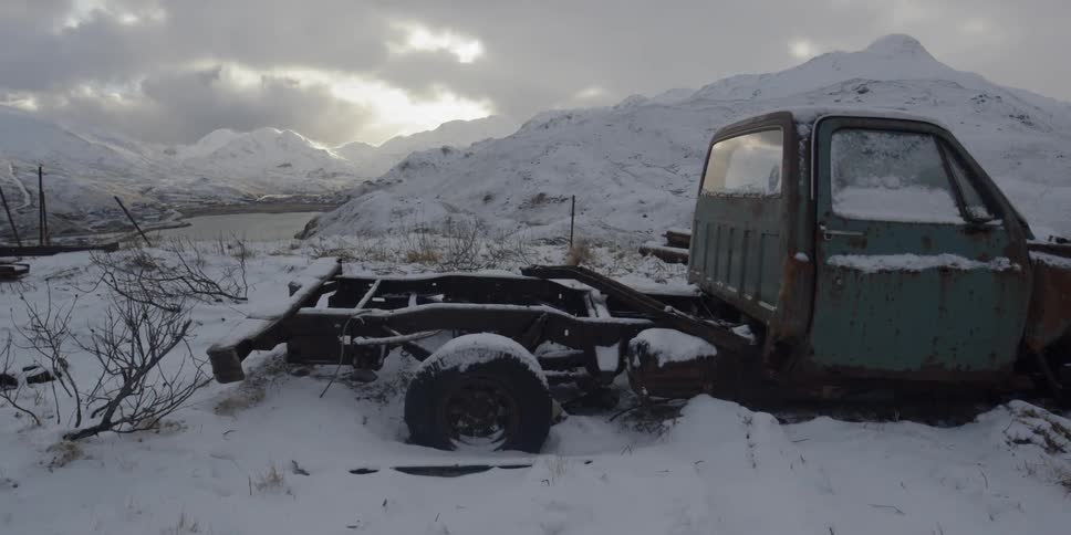 A rusted out truck is partially covered in snow