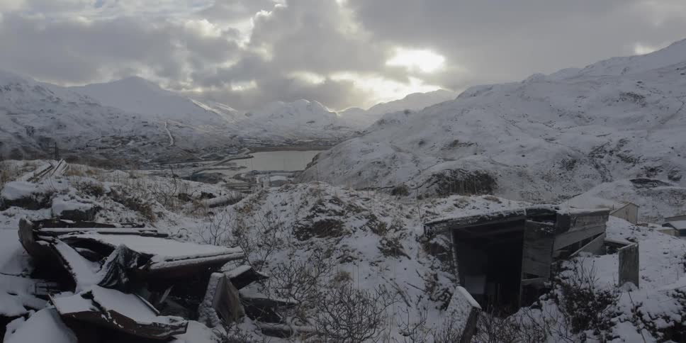 Snow covers hills and what remains of a shelter