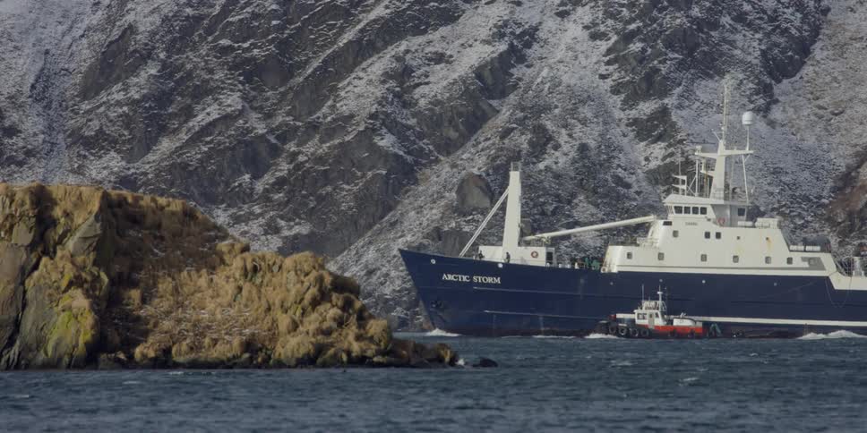 A large boat is sailing through the sea next to a mountain