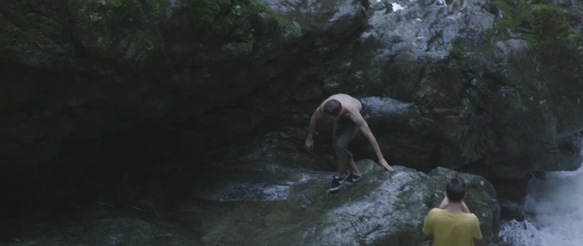 Man climbs down wet cliff with water below