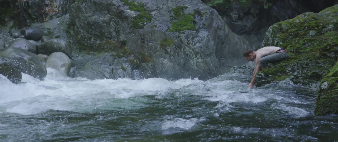 Man leaning over some rapids washing his hands in the water