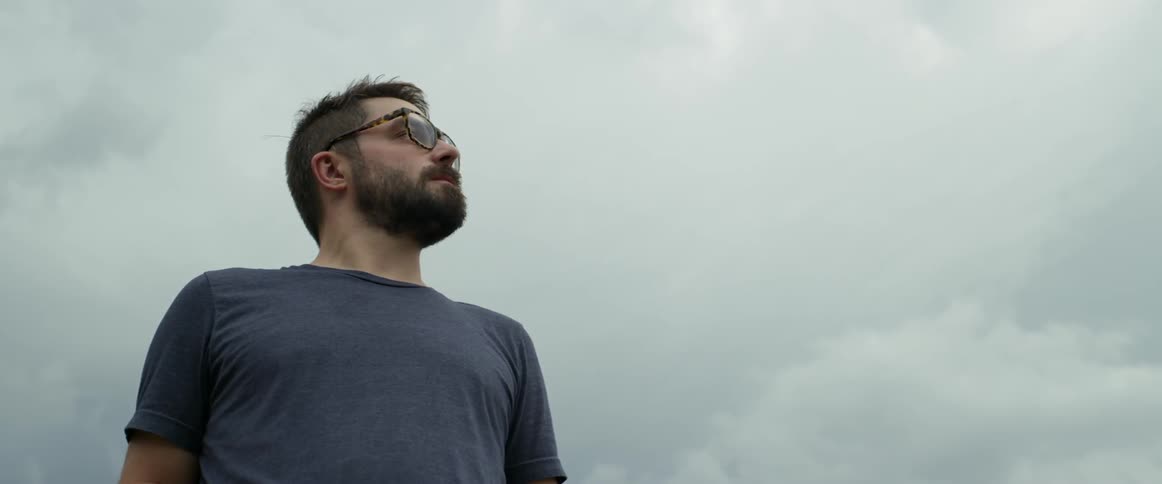 Bearded man wearing eyeglasses looking around outdoors on a cloudy day