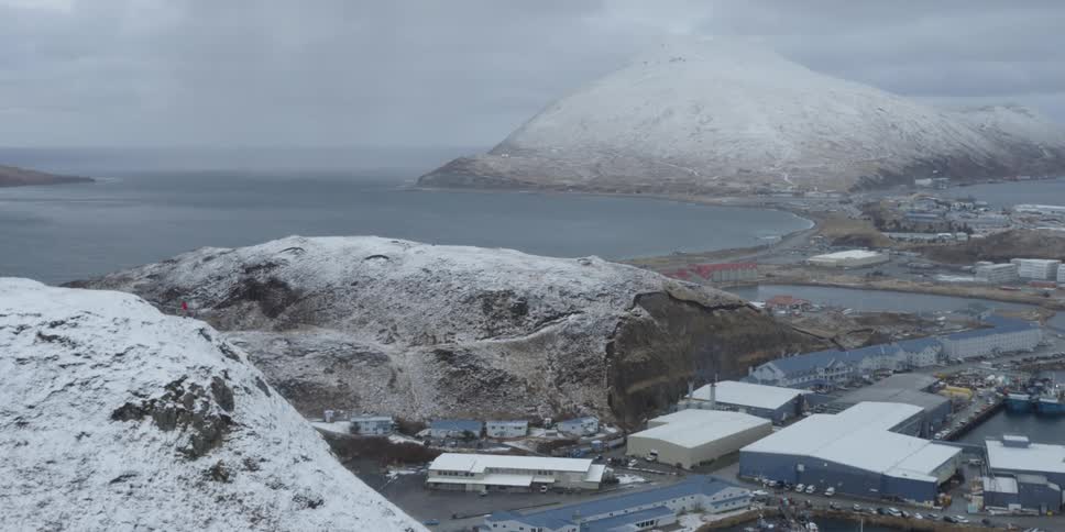 Snow covered hills and rock surround coastal buildings and road