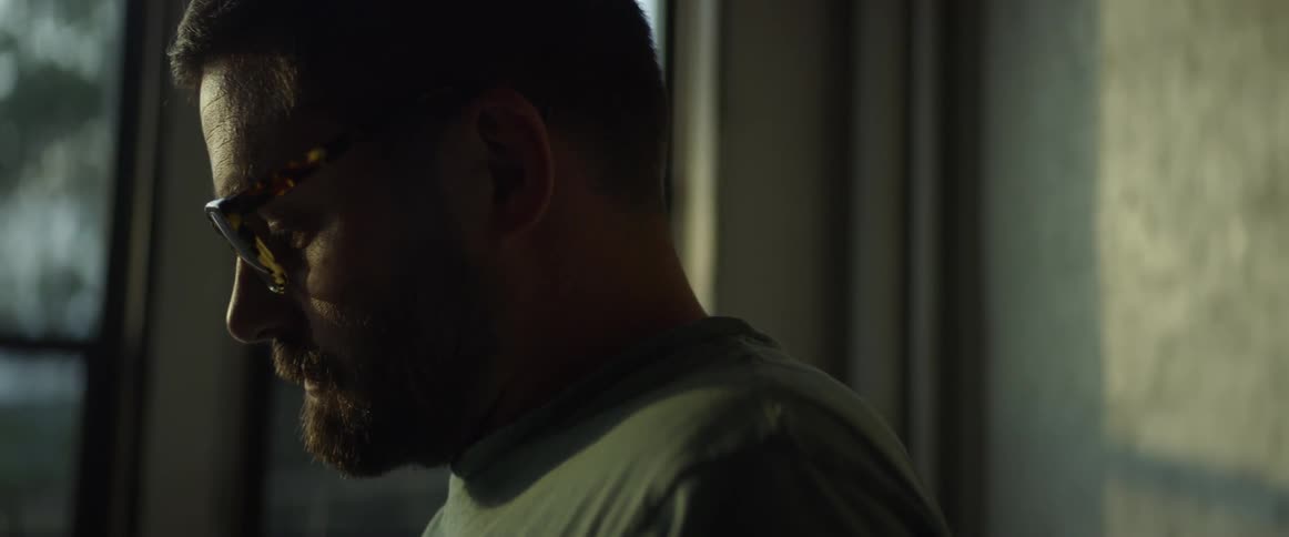 A man wearing glasses stares downward