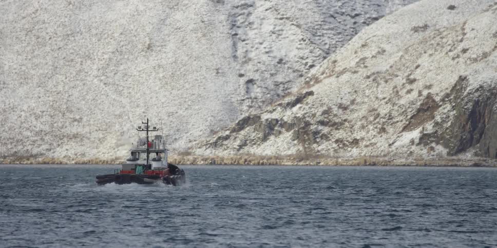 A boat travels on the cold waters by snowy mountains