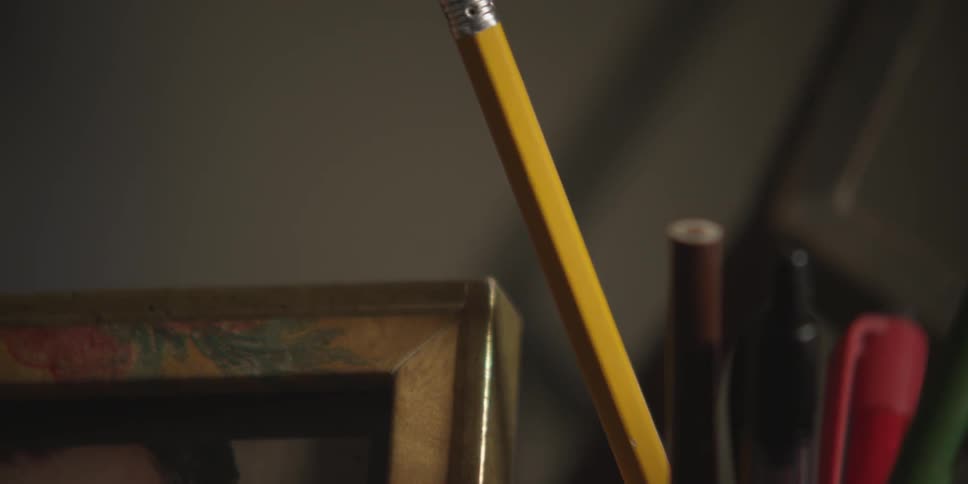 Pencils and pens are in a cup on a desk