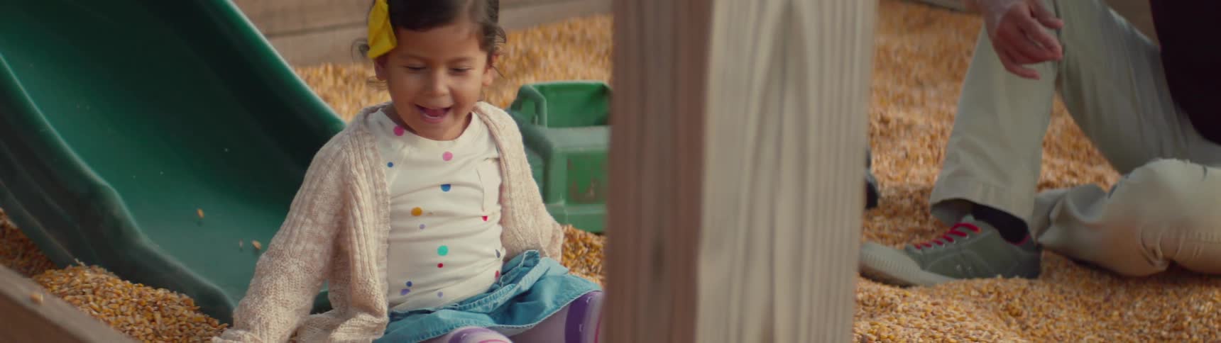 A little girl is sliding down a slide as her parents watch