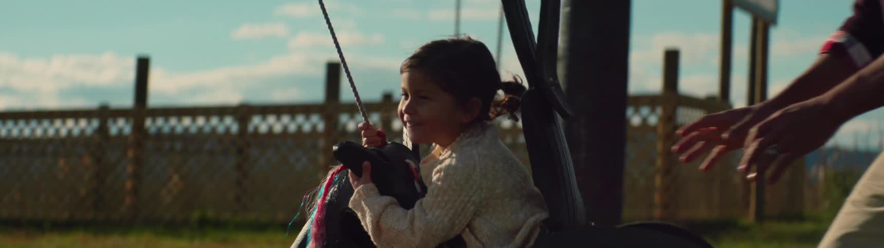 An father is pushing his child in a swing outside during the day
