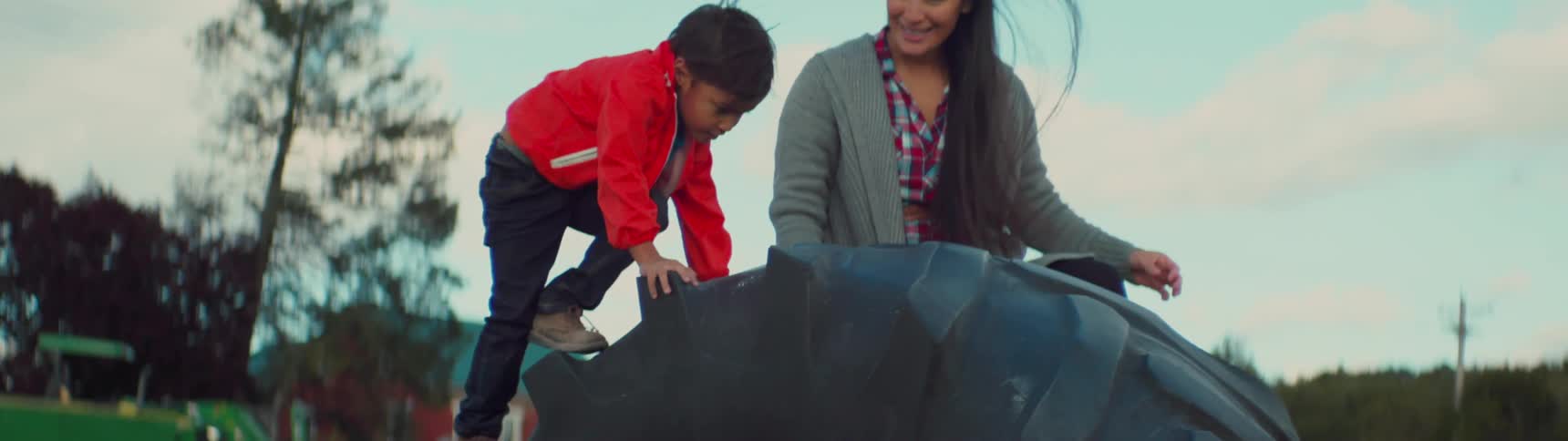 A mother is watching as her son climbs a large tire on a playground