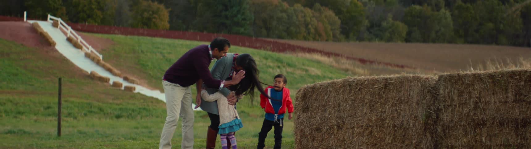 Family of four celebrating in a field next to some baled hay
