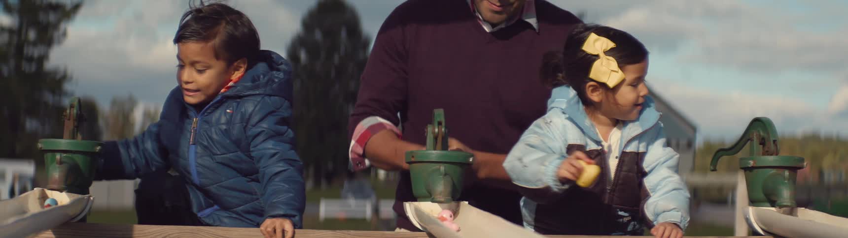 A man and his two children are playing outside with a water pump during the day