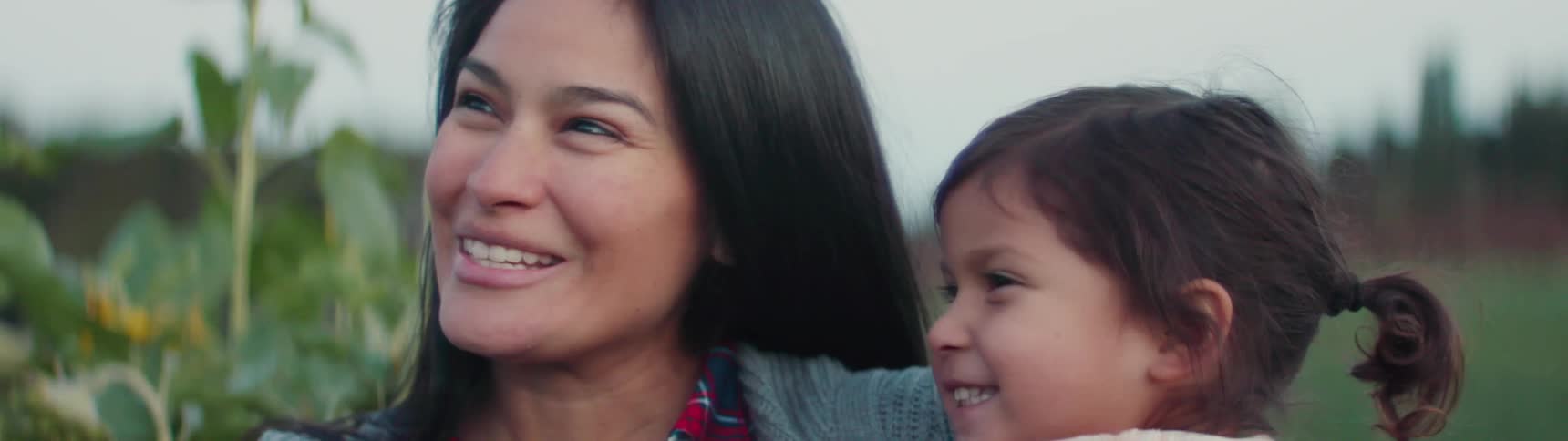 A woman and child smile while looking at a sunflower
