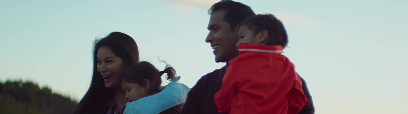 A couple are carrying their children as they walk outside during the day