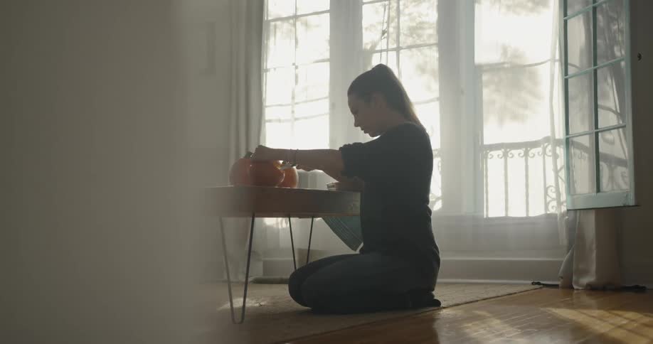A woman carves pumpkins while kneeling on the floor